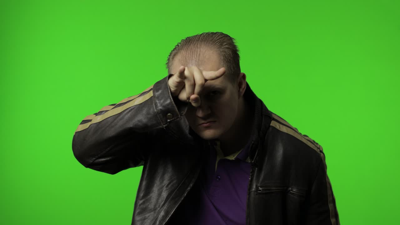 Angry rocker man in brown denim jacket demonstrating bull horns gesture with fingers on head