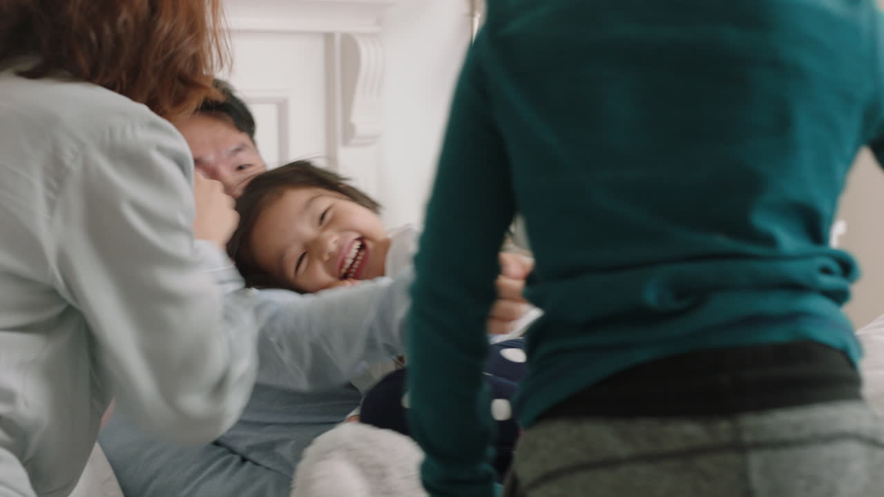행복한 아시아 가족과 아이들이 침대에 뛰어들고 엄마와 아빠와 함께 놀고 주말 아침에 재미를 느끼고 흥분된 어린 아이들이 부모와 함께 집에서 게임을 즐기고 있습니다. 4k 영상