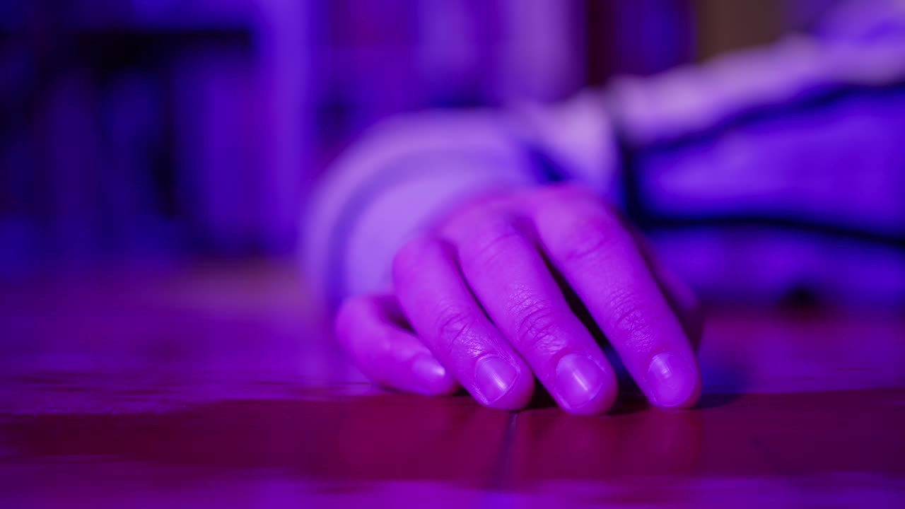 Mano umana appoggiata su un tavolo sotto una luce al neon viola