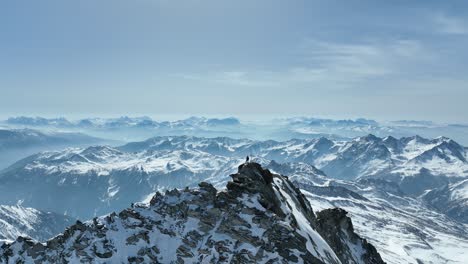 Drone-shot-of-a-person-standing-on-a-rocky-peak-in-the-Alps