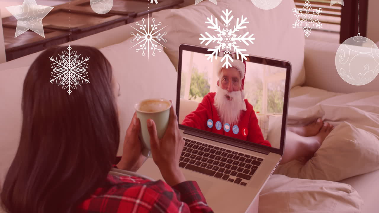 animación de nieve cayendo sobre una mujer biracial en una llamada de video portátil con papá noel en navidad