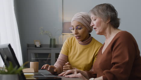 arabic woman teaching an elderly woman to use a laptop