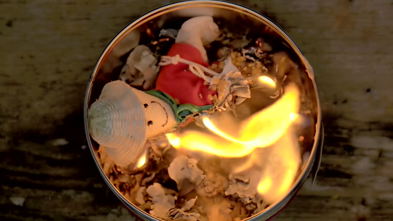 Sorcery witchcraft voodoo ritual with a doll being burned inside a bowl with fire to make a curse spell with him.  Muñeco de año viejo