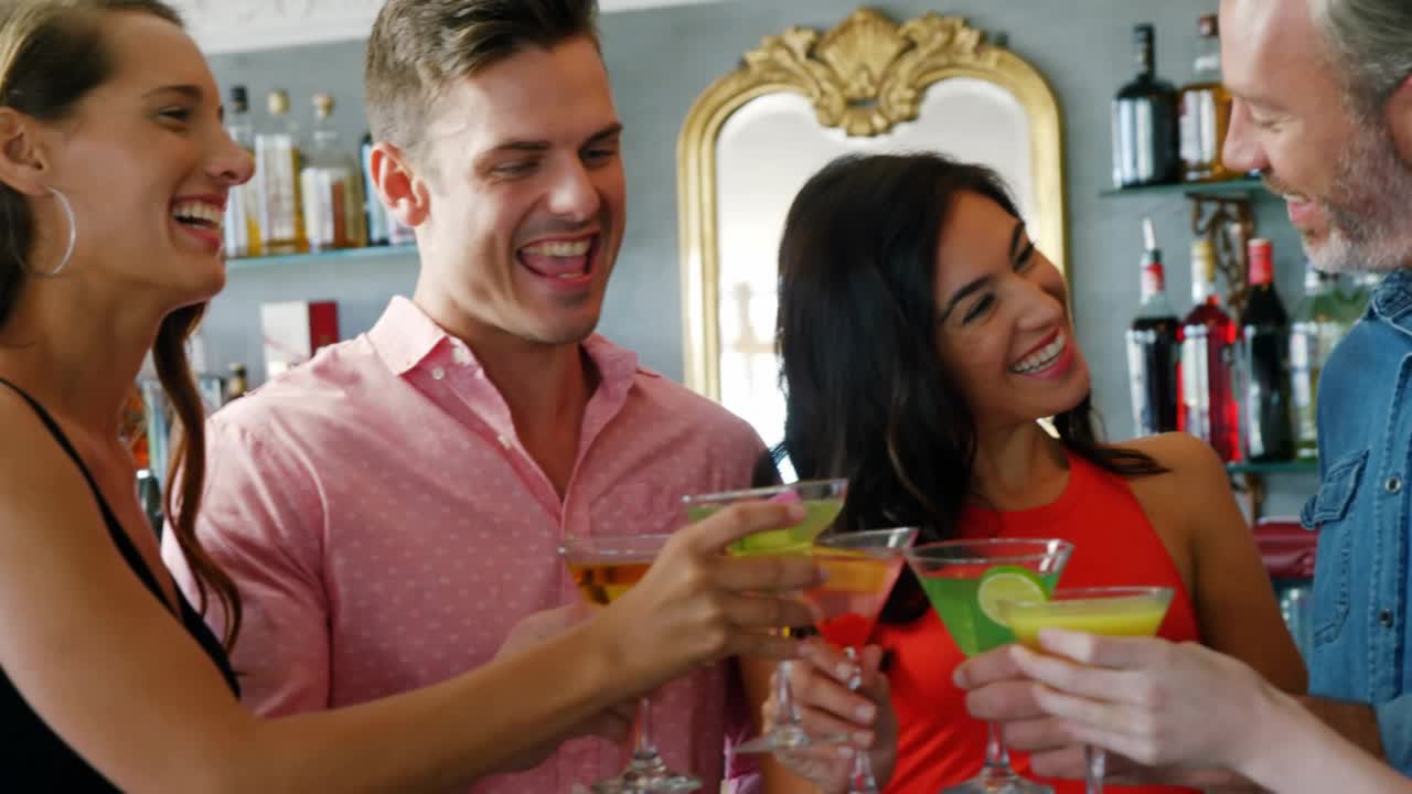 Group of five friends clinking glasses at social bar celebrating and sending hearts rising inward