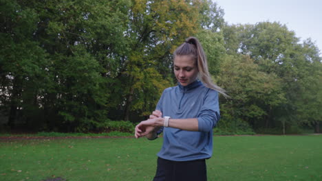 Captivating-shot-of-a-woman-stopping-mid-run-in-a-grassy-field-at-the-park-to-check-her-digital-sports-watch