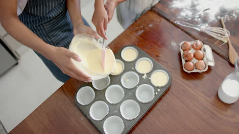 overhead of biracial mother and daughter pouring cake mix into forms, copy space, slow motion