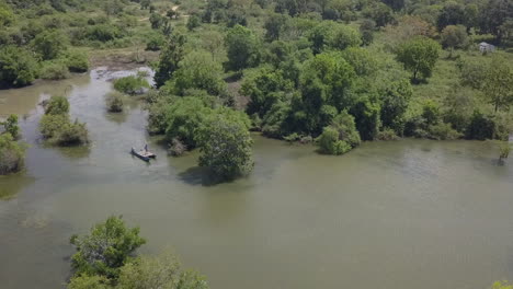 jungle aerial descends to men paddling canoe raft in flooded swamp