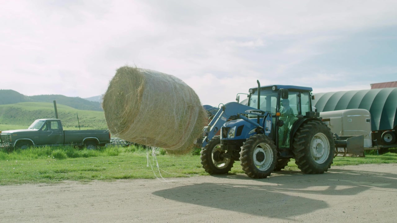 Trattore verde che trasporta una balla di fieno in un ranch al rallentatore