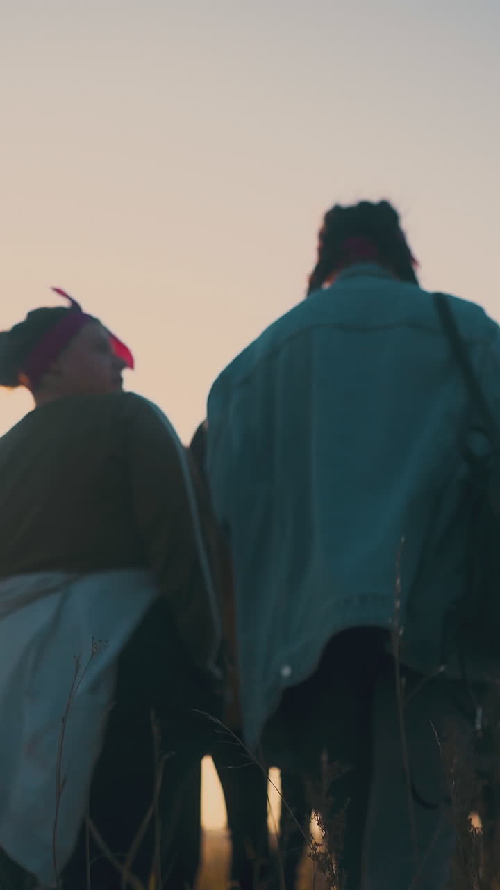 joyful men and women walk along grass field after day hike at autumn sunset backside low angle shot