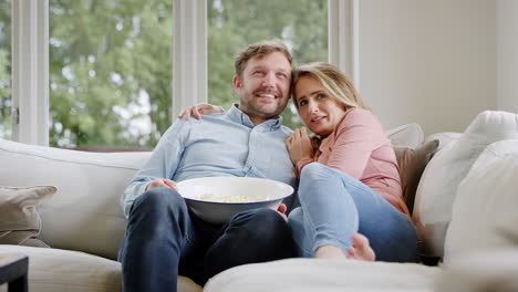 couple on date night sitting on sofa at home watching scary movie on tv with popcorn