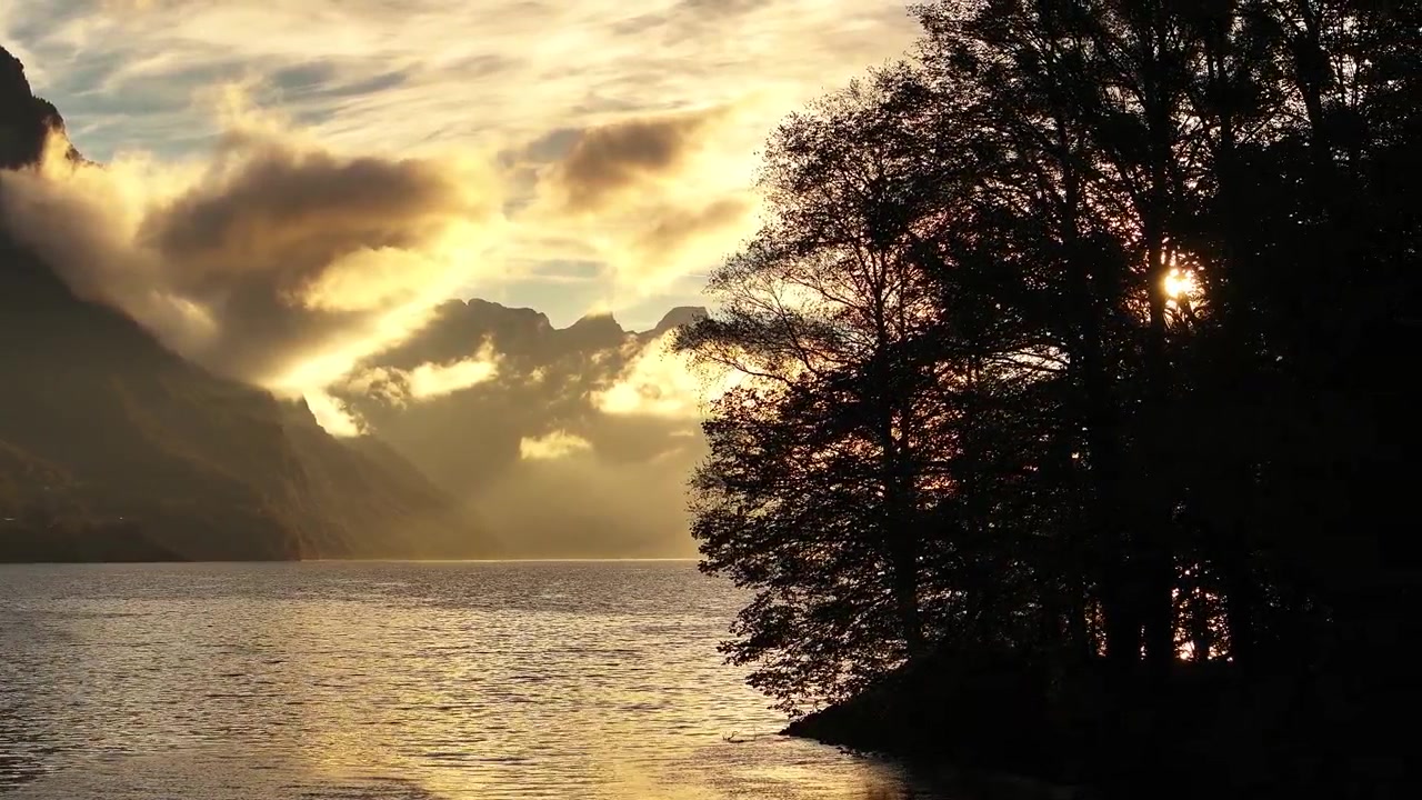 Golden sunset over Walensee, Switzerland, with glowing clouds, mountains, and silhouetted trees