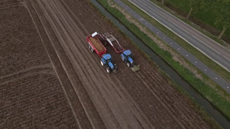 drone circle around tractors driving over farm land harvesting potato crop