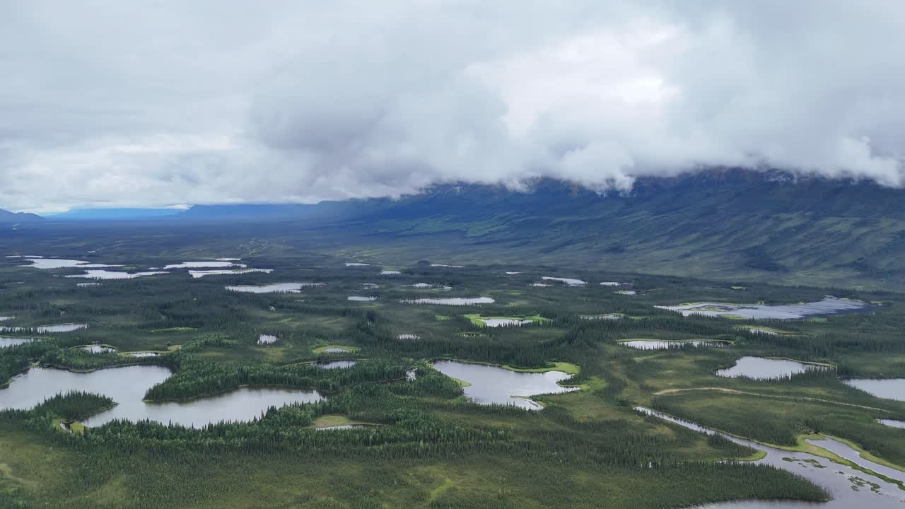 Breathtaking Alaskan landscape with many lakes surrounded by lush greenery and distant mountains shrouded in mist creates a serene natural panorama