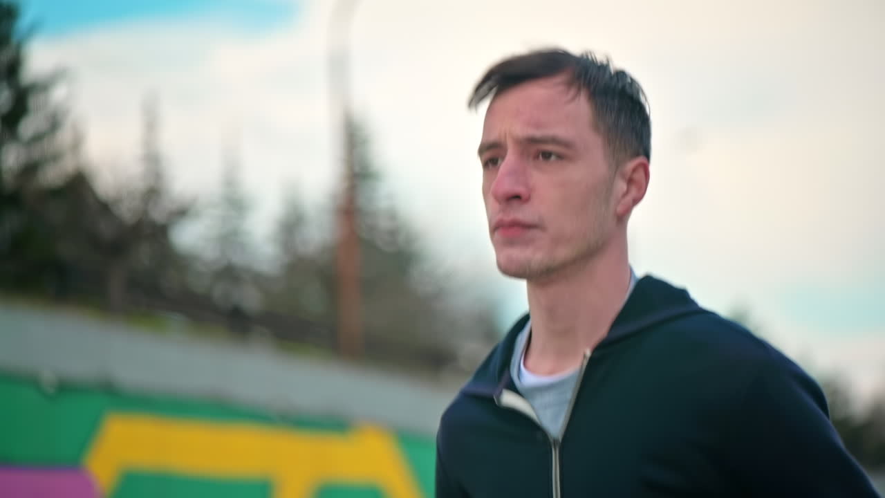 Young focused man running in jacket. Cloudy weather. Slow motion