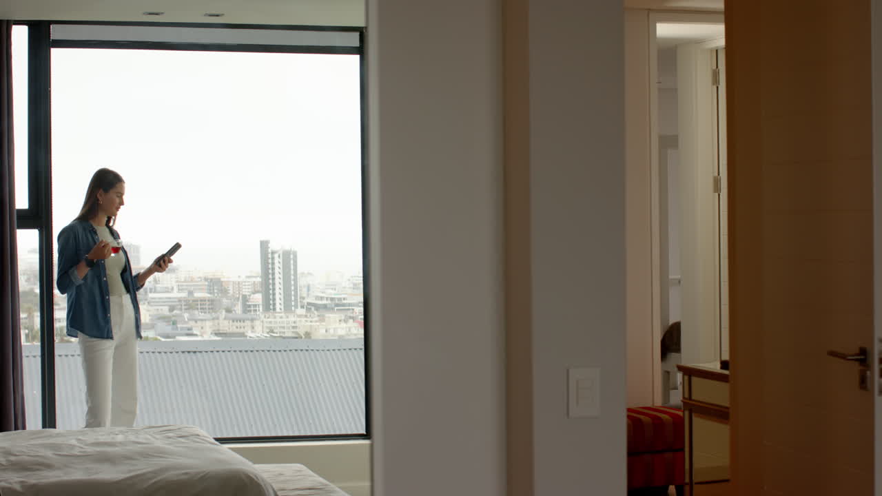 Holding smartphone, woman standing by window in modern home spa setting