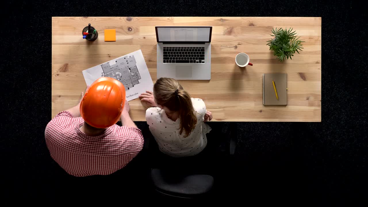 Young businesswoman discusses plan of building with builder, works on laptop in daytime, work concept, office concept, communication concept, top shot