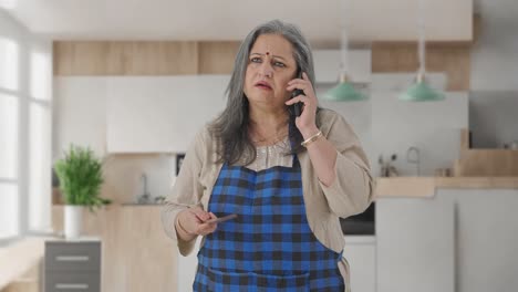 Indian-aged-housewife-talking-on-phone-while-cooking-food