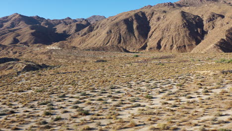 Low-drone-shot-over-floor-of-arid-landscape-approaching-close-barren-mountains