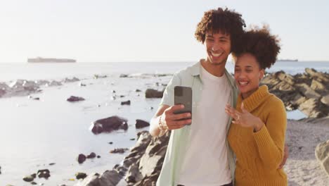 Pareja-Afroamericana-Tomándose-Una-Selfie-Y-Mostrando-Su-Anillo-Parado-En-Las-Rocas-Cerca-Del-Mar