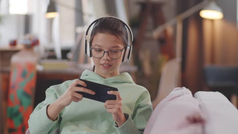 una adolescente jugando a un juego en su teléfono inteligente en casa