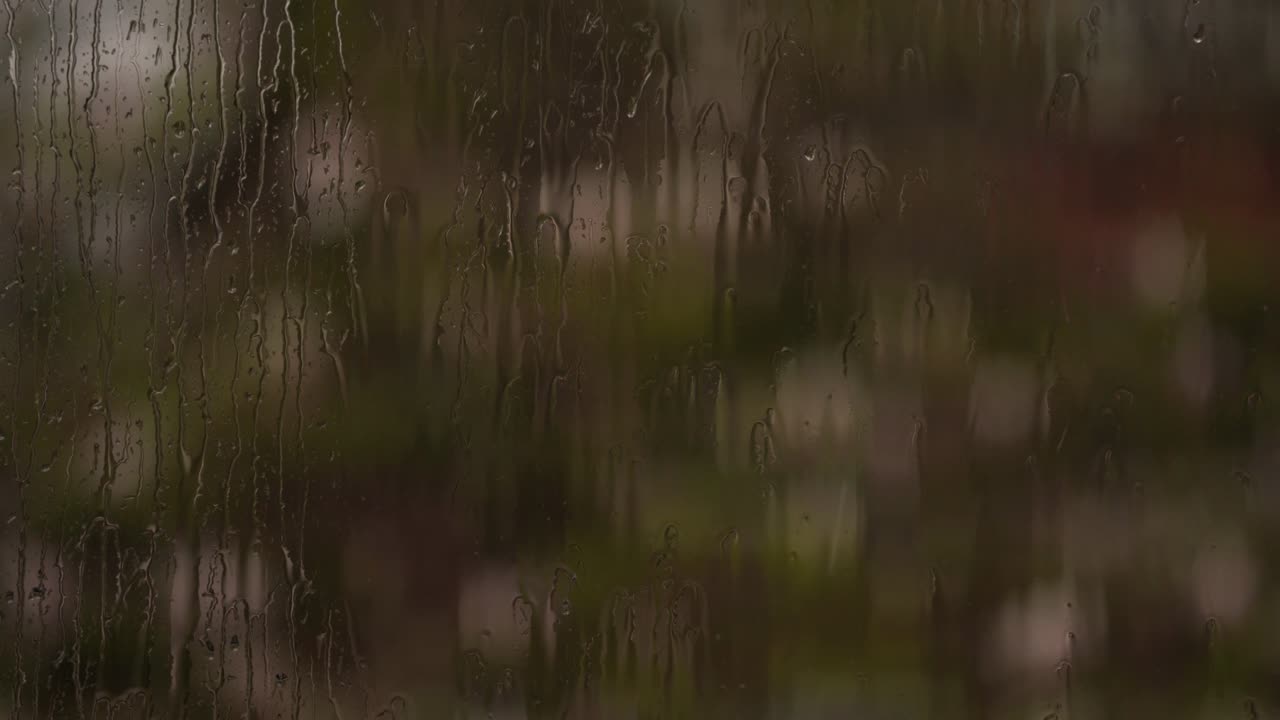 Raindrops against a window with white flowers moving in the wind in the background