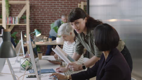 senior mixed race business woman using computer in modern office young female intern showing chart data pointing at screen diverse team collaborating in workspace