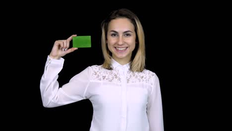 young businesswoman in a white shirt holds a bank card in her hand. isolated black background. chromakey green card.