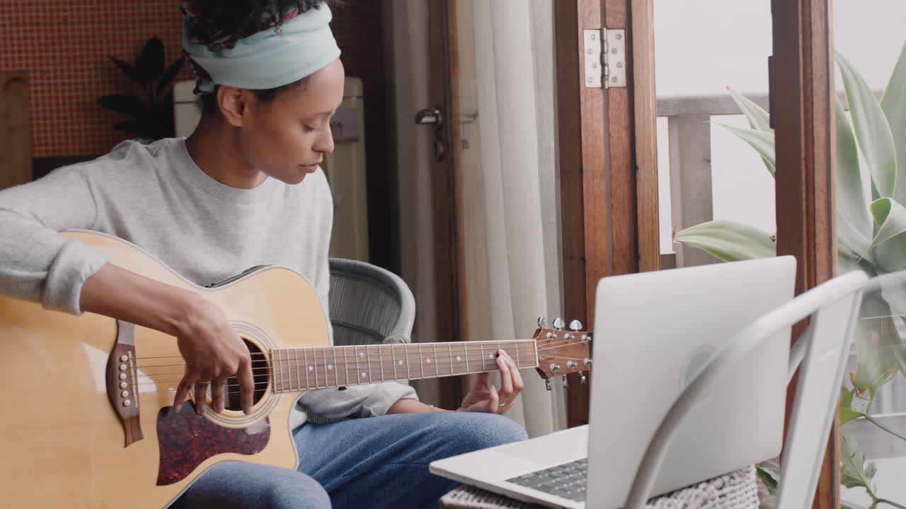 giovane donna che suona la chitarra a casa aspirante musicista che impara a suonare uno strumento musicale usando il portatile che gode dell'espressione creativa che pratica la musica