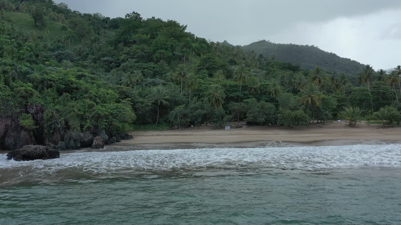 vuelo de descenso aéreo hacia palmeras de la selva y playa de arena con olas del mar caribe durante el día oscuro - playa elvalle, república dominicana