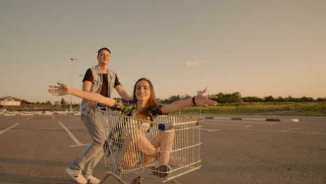 una joven pareja romántica se está divirtiendo con el carrito del supermercado por la noche. un hermoso hombre barbudo y una joven atractiva están pasando tiempo juntos al aire libre.