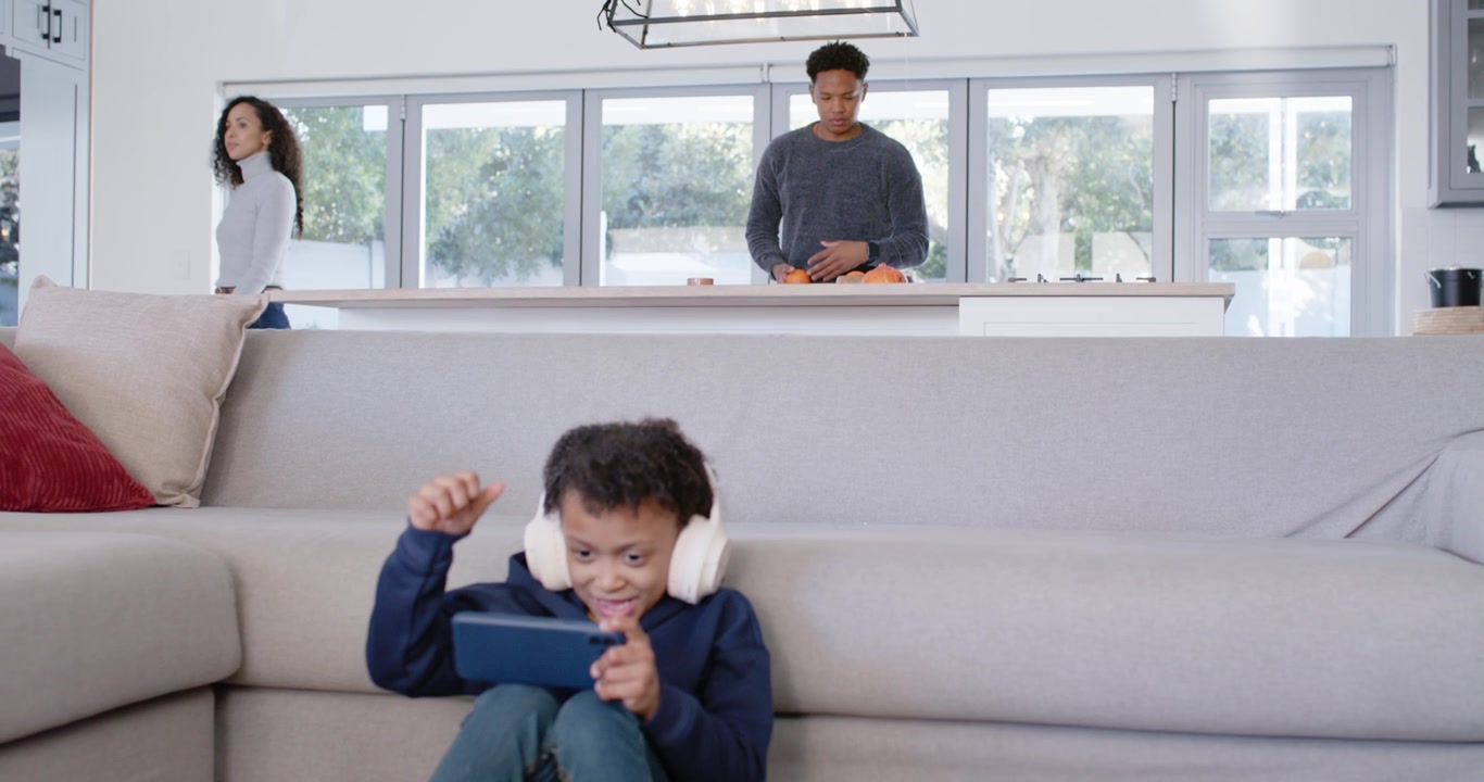 African American child sitting home wearing headset, on device, reacting onscreen