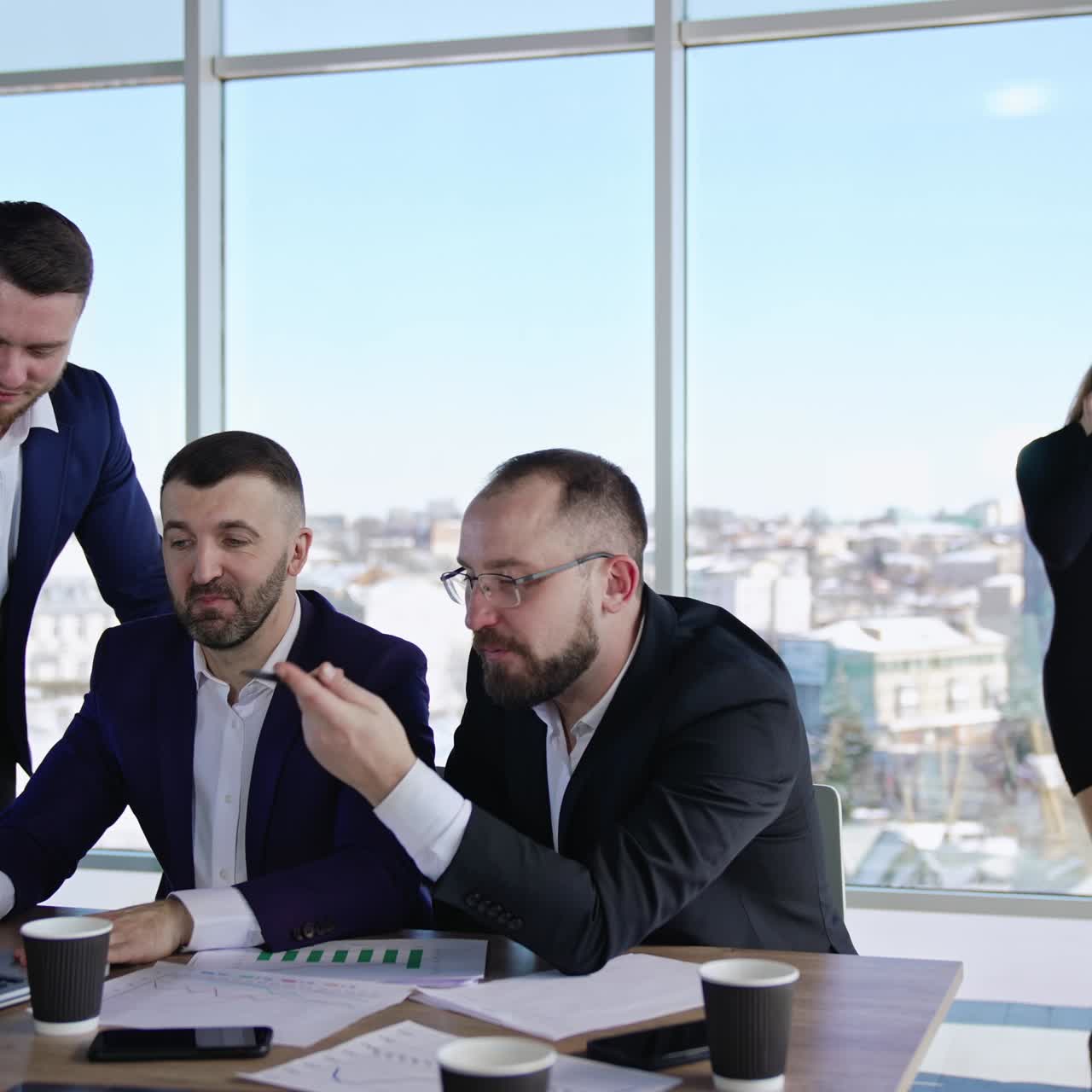 Male colleagues sitting at the table building strategies and discussing something in front of laptop. Productive work in the big light office. Two female coworkers chatting at the backdrop