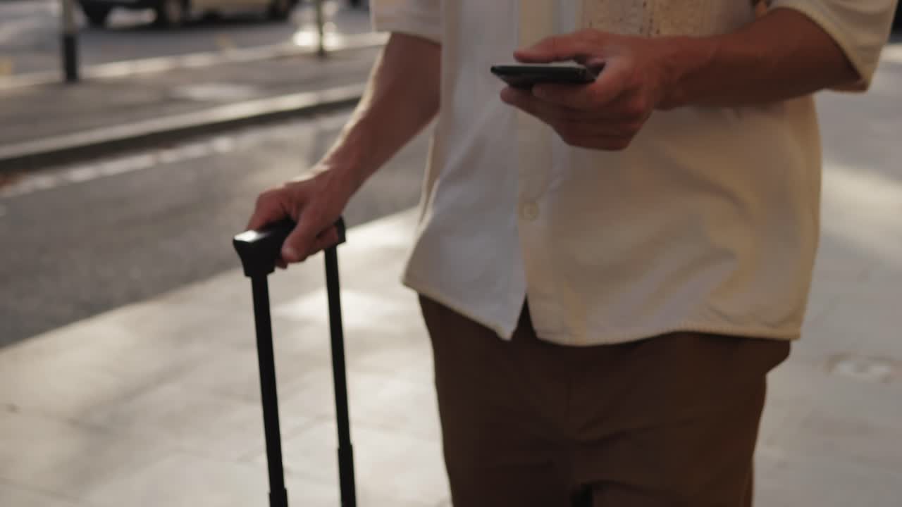Man using phone while pulling luggage on city street