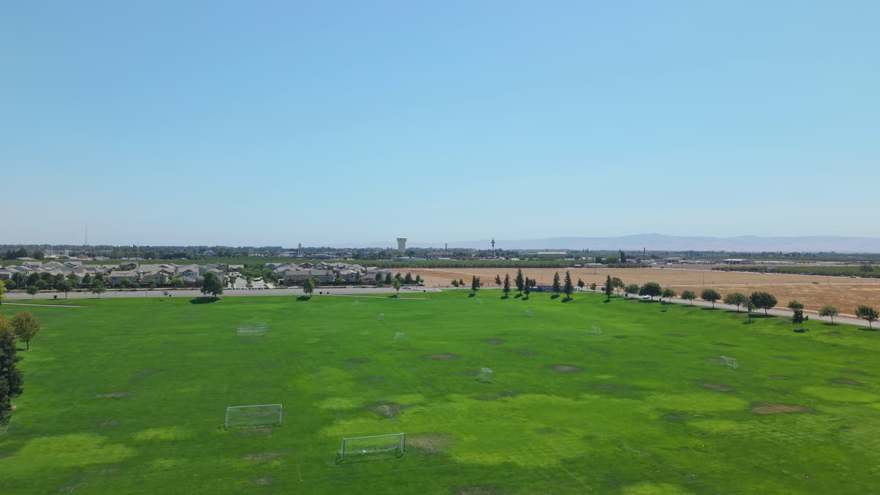 Drone ascending from soccer field into sky showing farmland and residential area