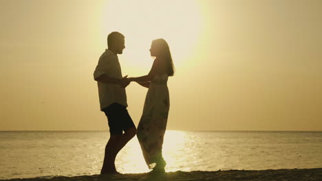 silhouettes of a young couple cool dancing against the backdrop of the sea and the setting sun merry