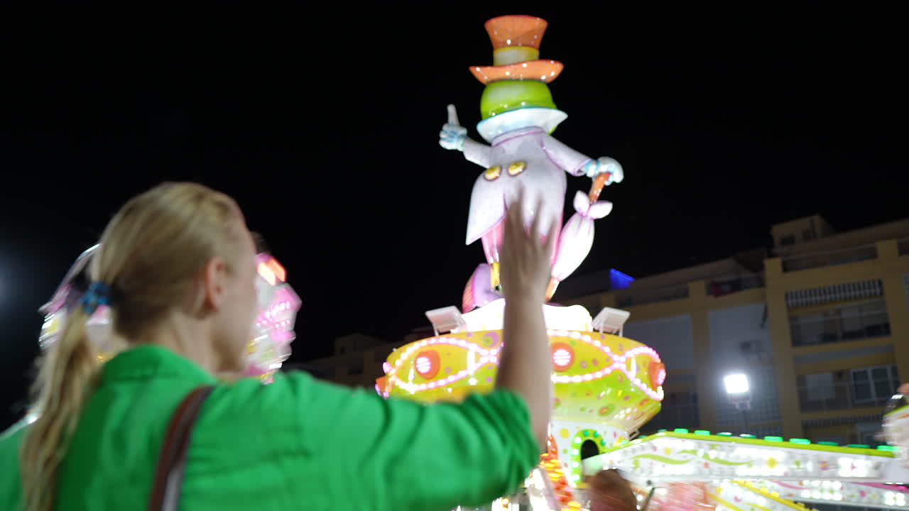 Woman Watching a Colorful Spinning Amusement Park Ride at Night