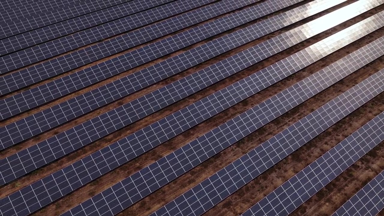 Droneoptagelser fra luften glider over rækker af solbeskinnede solpaneler på en italiensk solcellepark om sommeren, der fanger innovation inden for vedvarende energi, ren teknologi og klart, lyst naturligt lys.