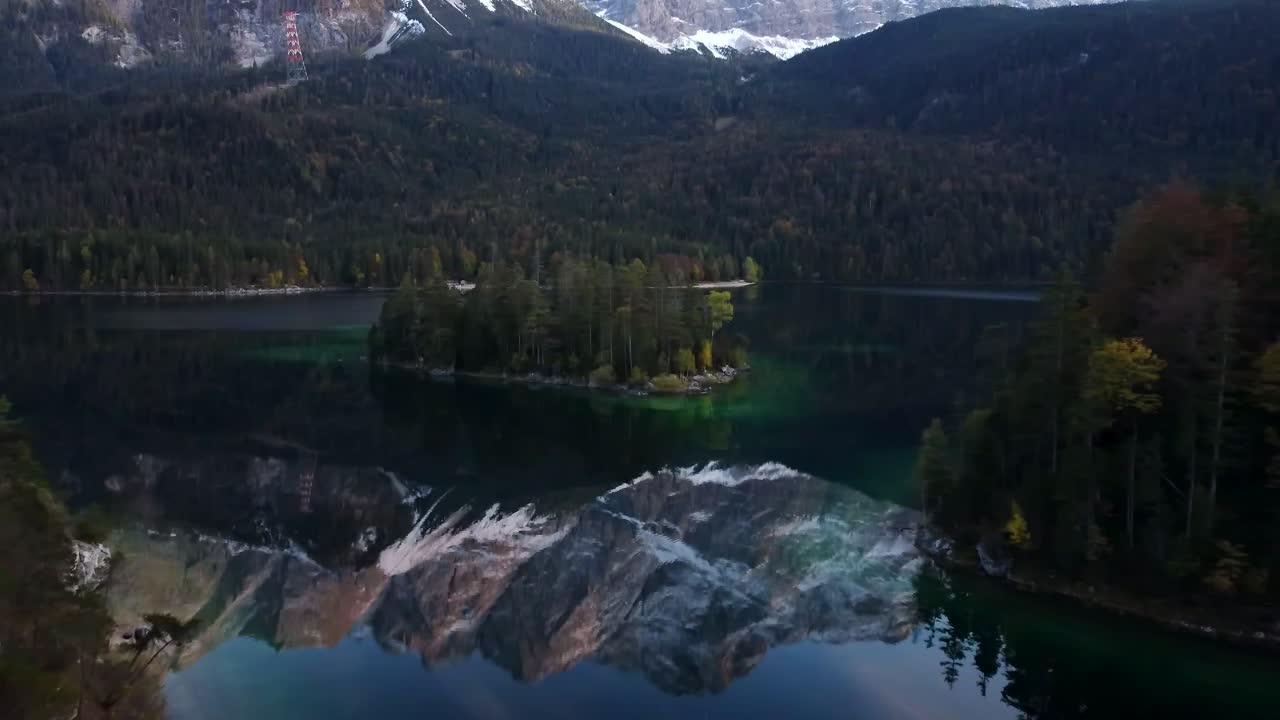 Sunset drone flight over Eibsee, while Zugspitze is reflecting in the lake, surrounded by autumnal trees