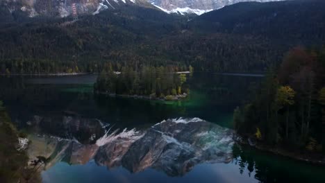 Vuelo-De-Drones-Al-Atardecer-Sobre-Eibsee,-Mientras-Zugspitze-Se-Refleja-En-El-Lago,-Rodeado-De-árboles-Otoñales