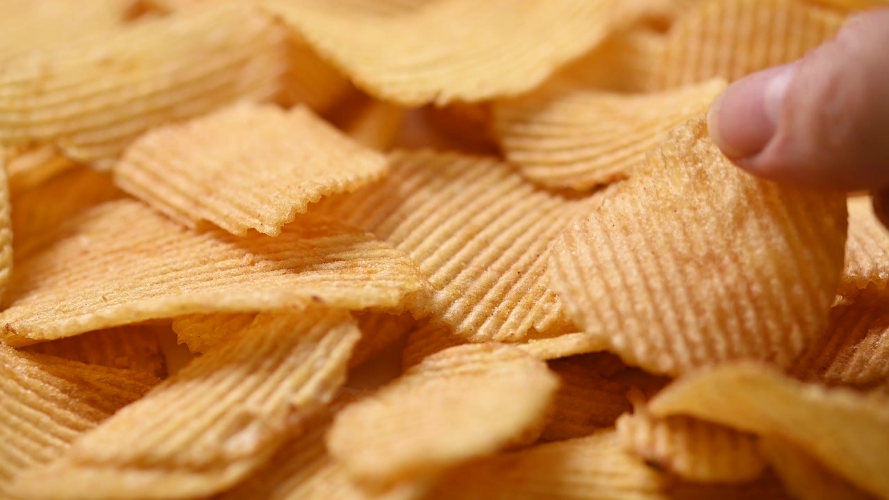Hånd tager fat i en sprød kartoffelchip.