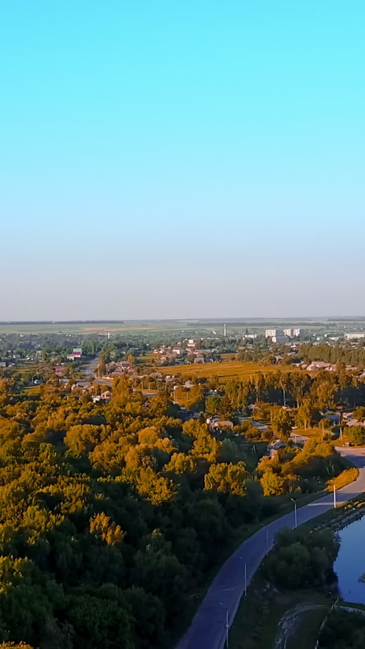 Breath-taking cityscape full of greenery on bright sunny day. River flowing along the provincial city from top view. Vertical video