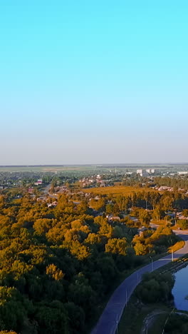 breath-taking cityscape full of greenery on bright sunny day. river flowing along the provincial city from top view. vertical video