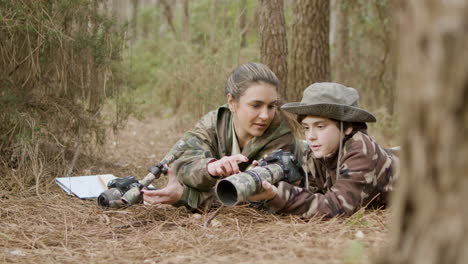 caucasian woman and her son birdwatching while lying on the ground in the forest