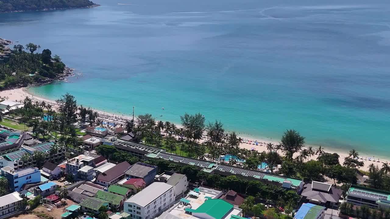 Aerial footage capturing Phuket's sandy beach, vibrant turquoise waters, and nearby buildings under clear skies.