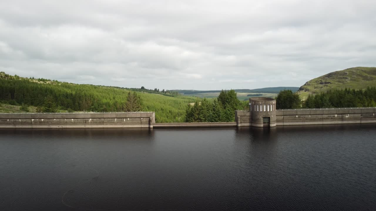 Drone footage flying over a dam wall and trees in the countryside below