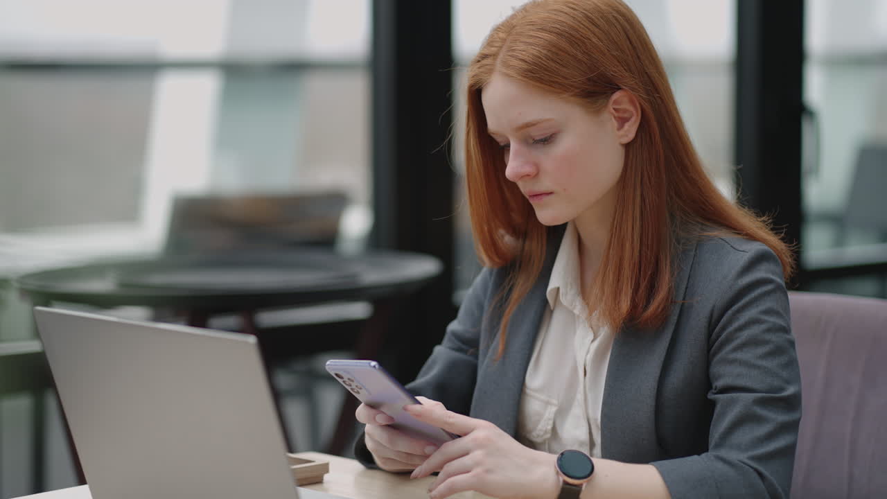 Young businesswoman use smart phone with laptop. Business woman in a modern office with a panoramic window sunny day laptop tablet use a mobile phone in a situation