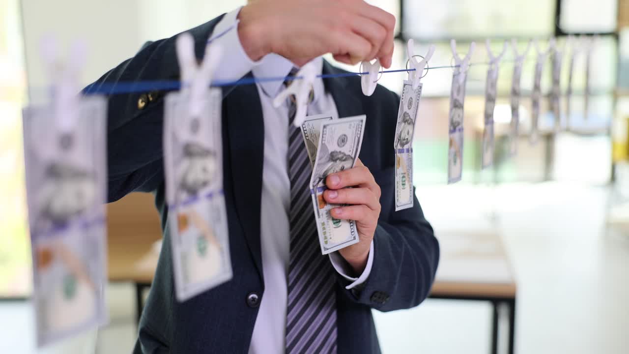 Biznesmen zdejmuje wysuszone banknoty dolarowe ze sznurka na pranie.