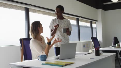 Two-diverse-female-colleagues-looking-at-laptop-and-discussing-in-office