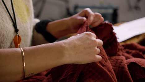 female caucasian fashion designer pinning together red fabric to make clothing in her studio