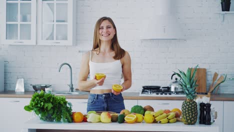 beautiful female in the light kitchen. smiling young woman proposing fresh orange. healthy organic fruit and vegetables on the table.